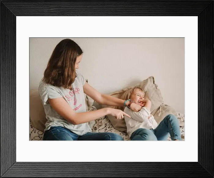 Framed Print : Cheerful teen girl sitting on bed and tickling laughing sister while playing together at home during weekend Framed Print : Cheerful teen girl sitting on bed and tickling laughing sister while playing together at home during weekend