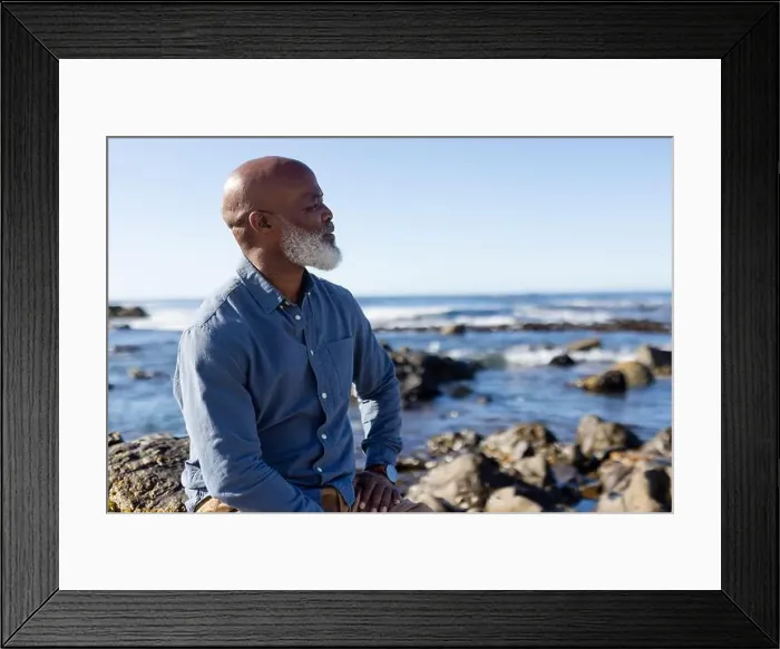 Framed Print : Thoughtful senior african american man sitting on rocks and admiring view at seaside Framed Print : Thoughtful senior african american man sitting on rocks and admiring view at seaside