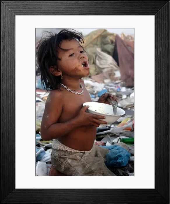 Framed Print : A hungry young child worker satisfies her hunger by eating a meal at The Stung Meanchey Landfill in Phnom Penh Framed Print : A hungry young child worker satisfies her hunger by eating a meal at The Stung Meanchey Landfill in Phnom Penh
