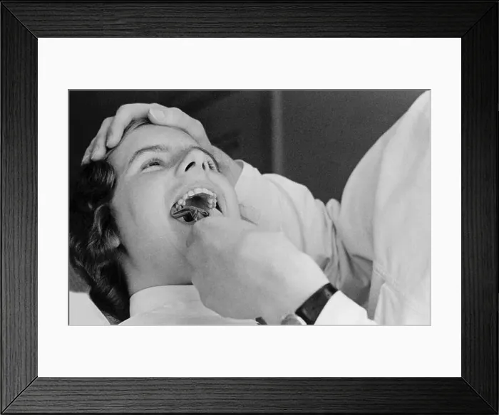 Framed Print : At the dentist in the 1940s. A woman patient is having one of her teeth pulled Framed Print : At the dentist in the 1940s. A woman patient is having one of her teeth pulled