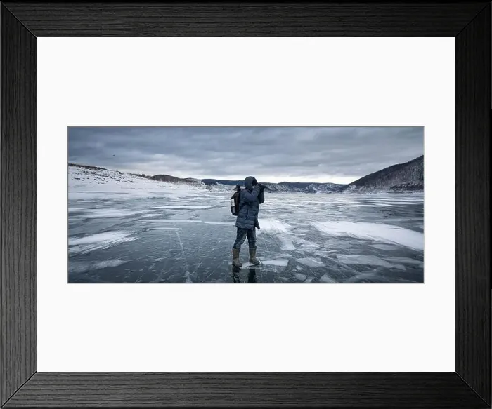 Framed Print : Person in winter gear explores and photographs the icy surface of a winter lake surrounded by snowy hills Framed Print : Person in winter gear explores and photographs the icy surface of a winter lake surrounded by snowy hills