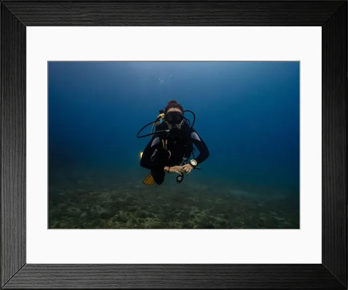 Framed Print : In this image, a female diver is depicted swimming underwater in a clear blue ocean environment Framed Print : In this image, a female diver is depicted swimming underwater in a clear blue ocean environment