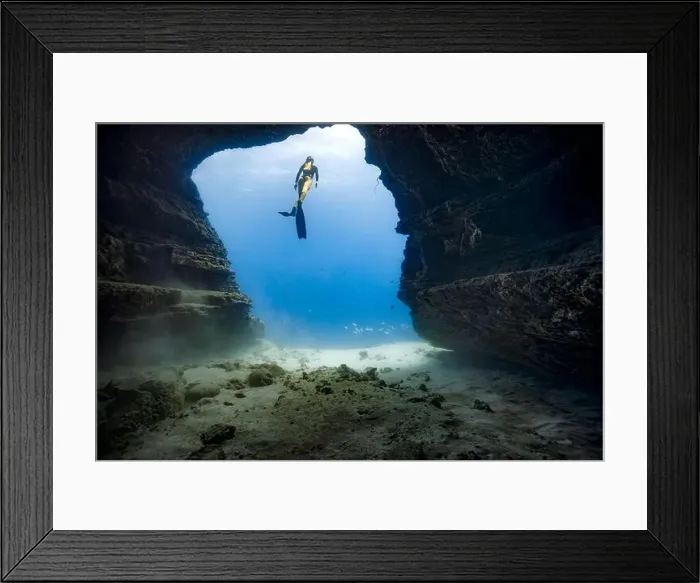 Framed Print : A young female free diving down into a cave doorway in the clear blue waters of Hawaii framed by shadowy cave walls Framed Print : A young female free diving down into a cave doorway in the clear blue waters of Hawaii framed by shadowy cave walls