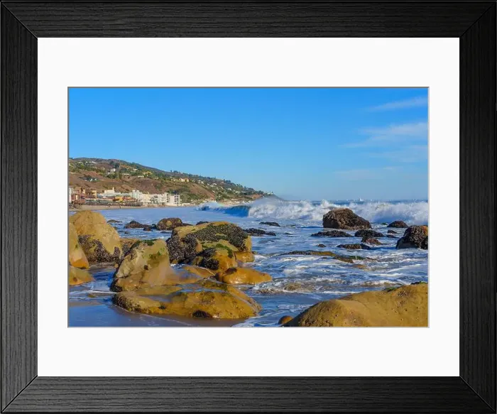 Framed Print : Dynamic waves crashing against rugged rocks at Malibu Beach, with coastal homes dotting the background Framed Print : Dynamic waves crashing against rugged rocks at Malibu Beach, with coastal homes dotting the background