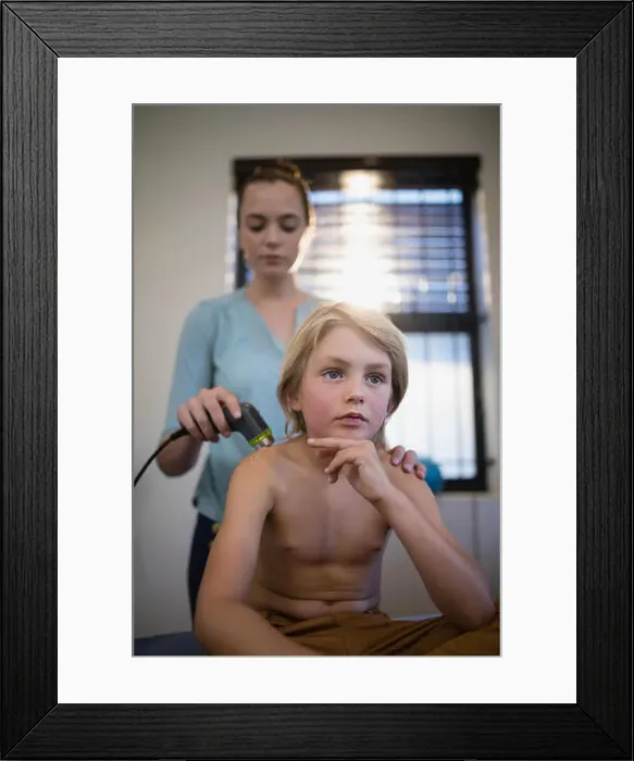 Framed Print : Thoughtful shirtless boy sitting with female therapist using ultrasound machine on shoulder at hospital ward Framed Print : Thoughtful shirtless boy sitting with female therapist using ultrasound machine on shoulder at hospital ward