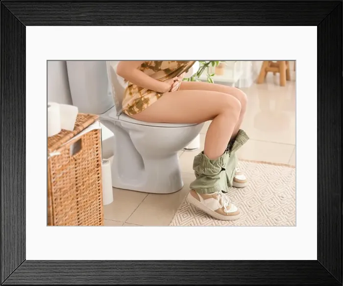 Framed Print : Young woman sitting on toilet bowl in restroom Framed Print : Young woman sitting on toilet bowl in restroom