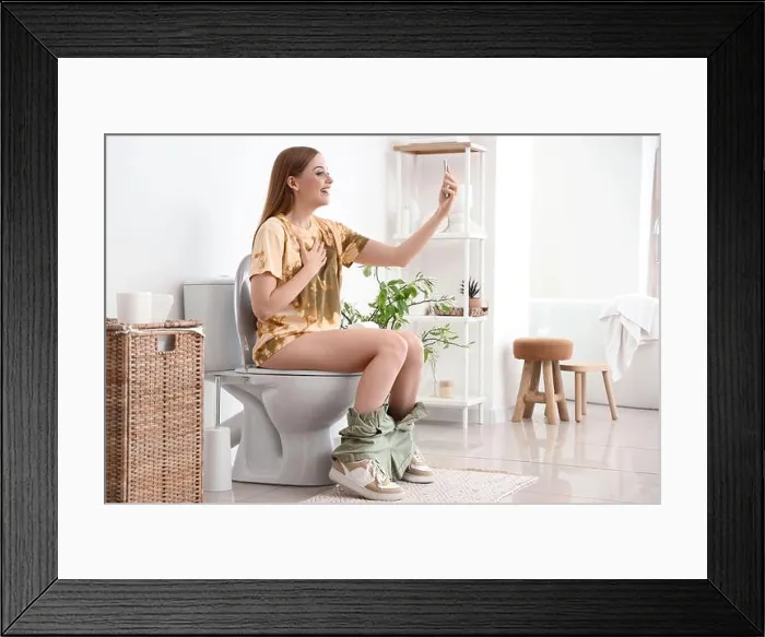 Framed Print : Young woman with mobile phone sitting on toilet bowl in restroom Framed Print : Young woman with mobile phone sitting on toilet bowl in restroom