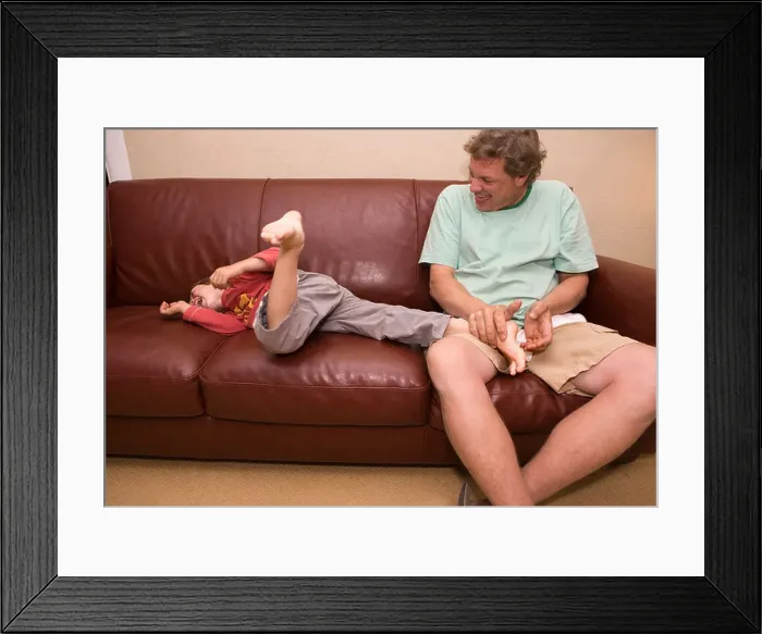Framed Print : father tickling five year old son at home on couch Framed Print : father tickling five year old son at home on couch