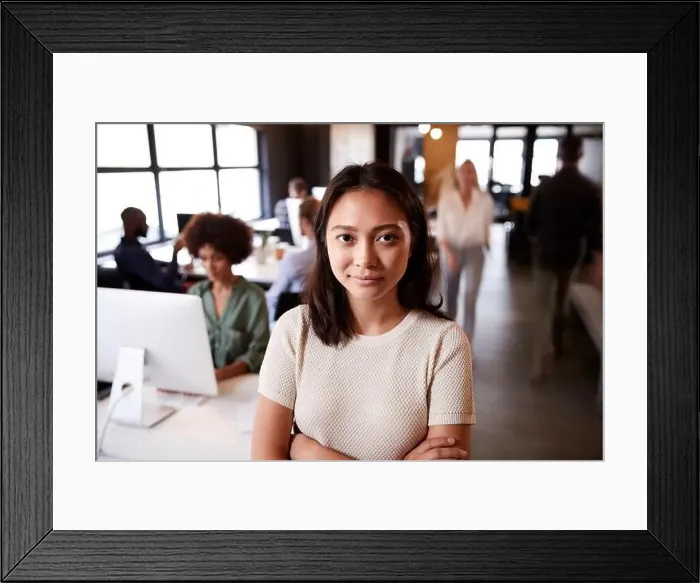 Framed Print : Millennial Asian female creative standing in a busy casual office, smiling to camera Framed Print : Millennial Asian female creative standing in a busy casual office, smiling to camera