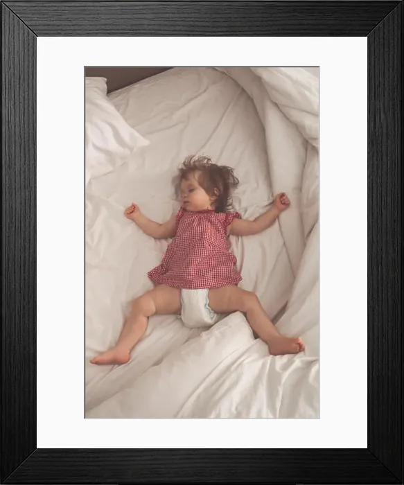 Framed Print : Baby girl sleeping on back with open arms and without pacifier in a bed with white sheets Framed Print : Baby girl sleeping on back with open arms and without pacifier in a bed with white sheets