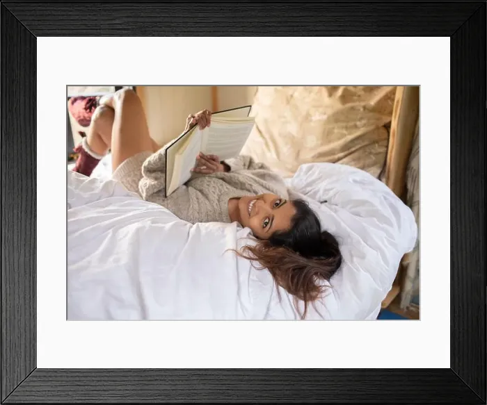 Framed Print : Portrait happy young woman relaxing with book in bed Framed Print : Portrait happy young woman relaxing with book in bed