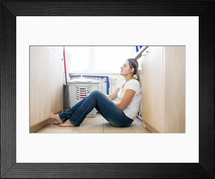 Framed Print : Upset lonely housewife sitting on floor after doing laundry Framed Print : Upset lonely housewife sitting on floor after doing laundry