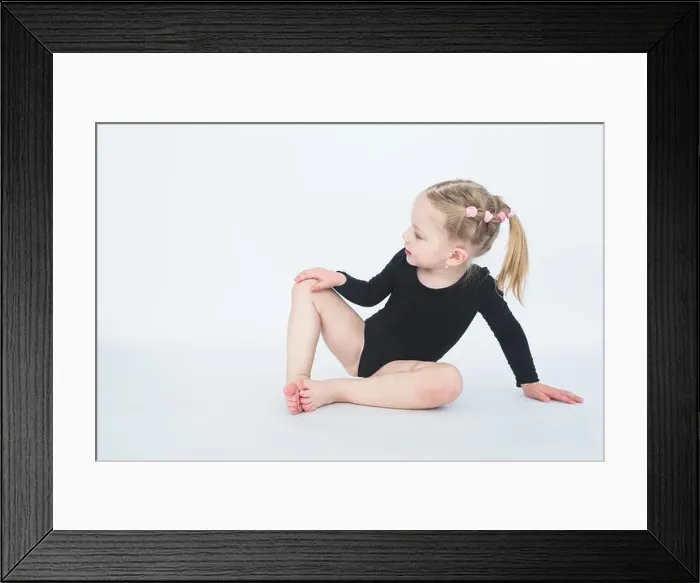 Framed Print : Cute little girl in beautiful black dress sitting on the floor on white background