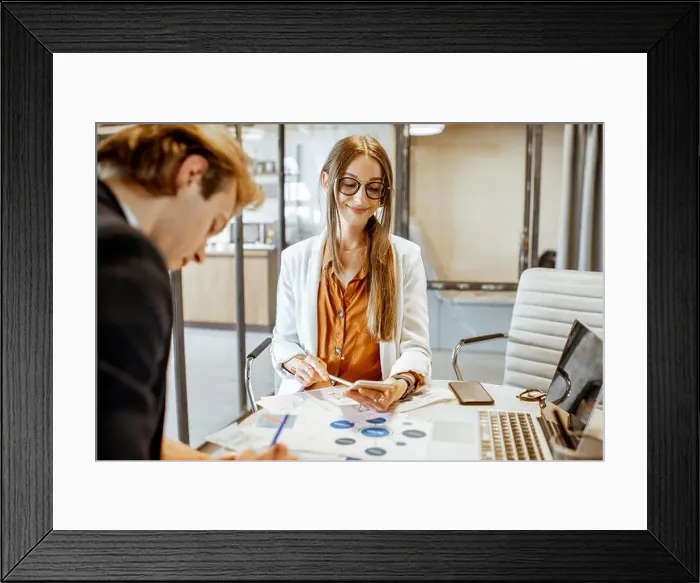 Framed Print : Young man and woman having a serious business conversation, working with paper documents and computer in the office Framed Print : Young man and woman having a serious business conversation, working with paper documents and computer in the office