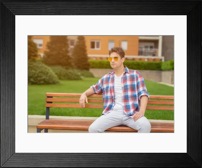 Framed Print : Young modern looking fashionable man posing by sitting on bench in the park Framed Print : Young modern looking fashionable man posing by sitting on bench in the park