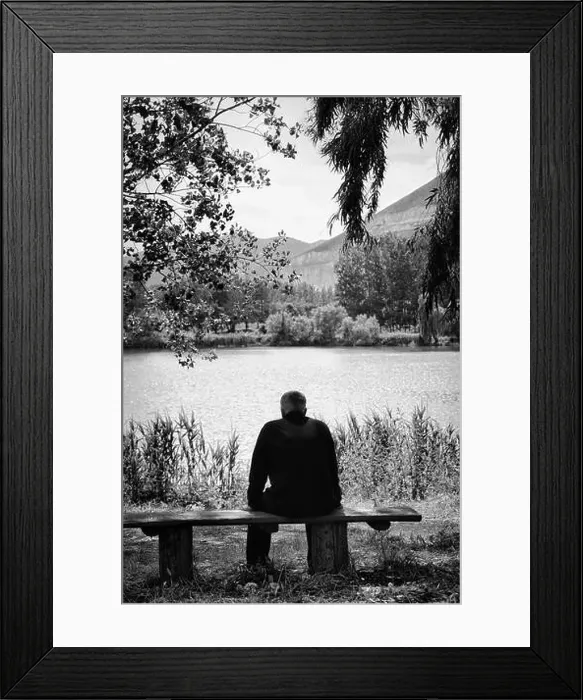 Framed Print : Man sitting on a bench overlooking the lake. Black and white image