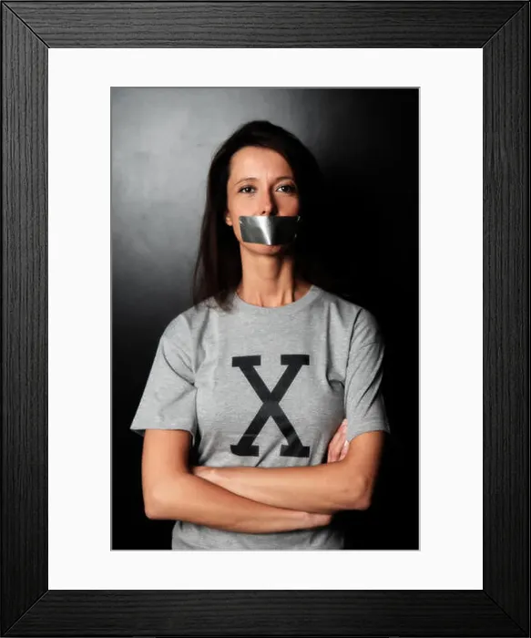 Framed Print : Femme brune en studio avec un tee-shirt avec un X et du scotch sur la bouche Framed Print : Femme brune en studio avec un tee-shirt avec un X et du scotch sur la bouche