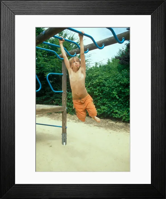 Framed Print : a young boy climbing along monkey bars on a playground Framed Print : a young boy climbing along monkey bars on a playground