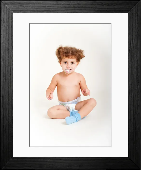 Framed Print : Young girl with pacifier, age 2, sits down on white canvas wearing diaper, blue socks Framed Print : Young girl with pacifier, age 2, sits down on white canvas wearing diaper, blue socks