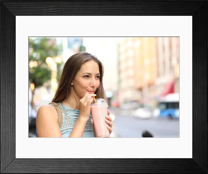 Framed Print : Pensive happy woman sipping a milkshake in the street Framed Print : Pensive happy woman sipping a milkshake in the street