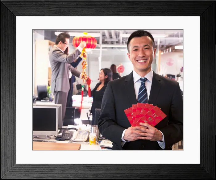 Framed Print : Businessman holding red envelopes and coworkers hanging decorations for Chinese new year