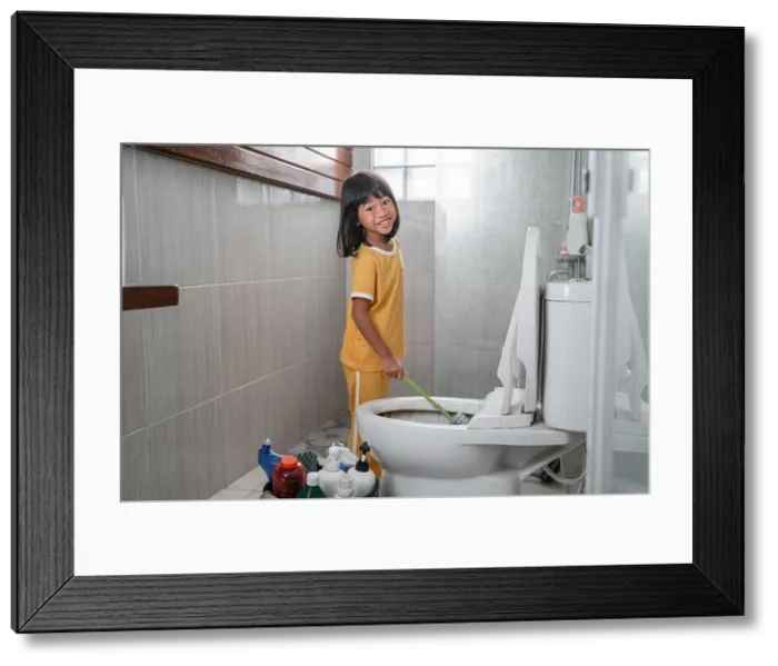 Framed Print : The little girl smiles at the camera while using the toilet brush to clean the dirty toilet Framed Print : The little girl smiles at the camera while using the toilet brush to clean the dirty toilet