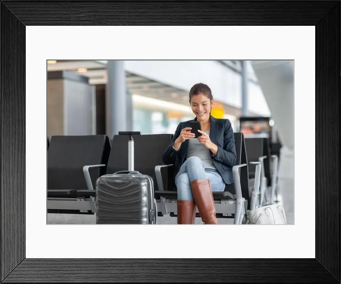 Framed Print : Travel airport woman using mobile phone waiting in lounge with hand luggage Framed Print : Travel airport woman using mobile phone waiting in lounge with hand luggage