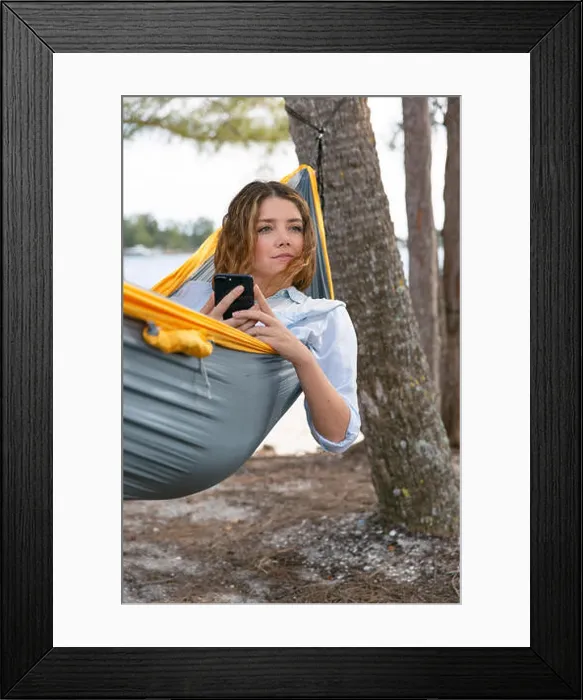 Framed Print : Young brunette woman hold her mobile phone while relaxing on a hammock Framed Print : Young brunette woman hold her mobile phone while relaxing on a hammock