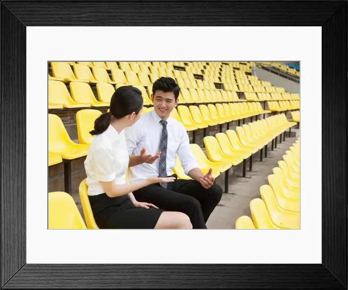 Framed Print : Businessman and businesswoman sitting on stadium seats talking with smiles