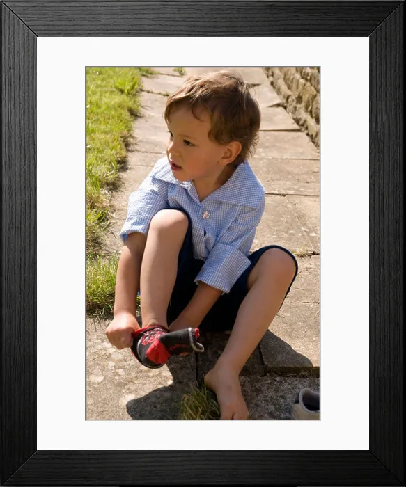 Framed Print : Little boy sitting on a stone path putting on a sock
