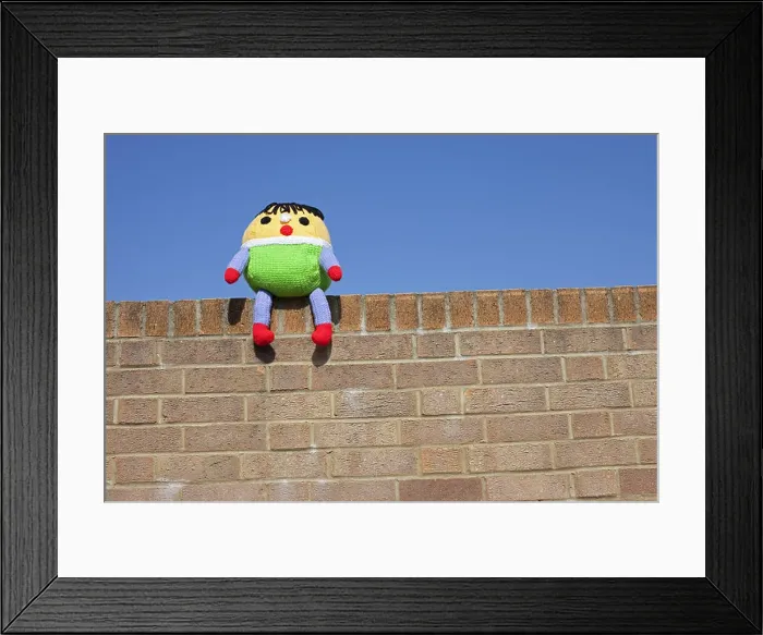 Framed Print : A Humpty Dumpty soft toy sat on the wall with a blue sky background Framed Print : A Humpty Dumpty soft toy sat on the wall with a blue sky background