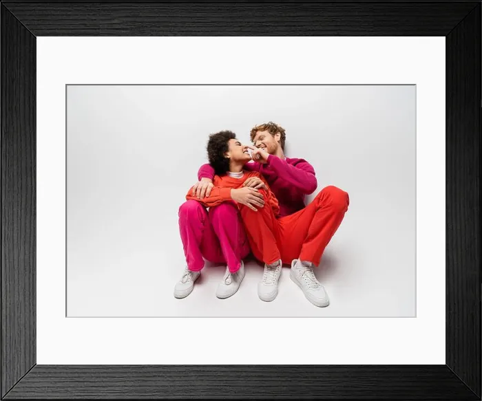 Framed Print : positive man toughing nose of african american woman in magenta color clothes sitting on white, stock image