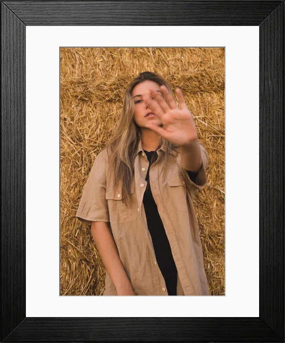 Framed Print : Young woman standing in front of hay bales making rejecting hand gesture, portrait Framed Print : Young woman standing in front of hay bales making rejecting hand gesture, portrait