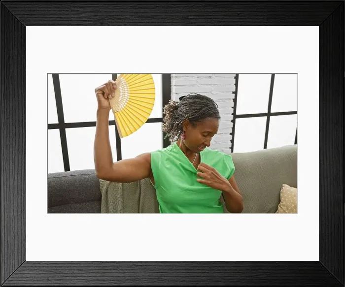 Framed Print : African american woman fanning herself indoors, feeling hot despite the home's modern, bright interior Framed Print : African american woman fanning herself indoors, feeling hot despite the home's modern, bright interior