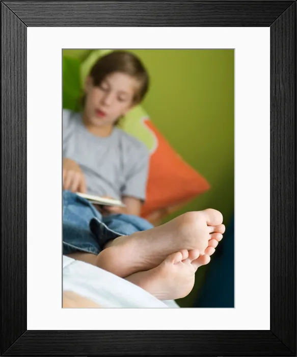 Framed Print : Boy reclining with feet up reading book