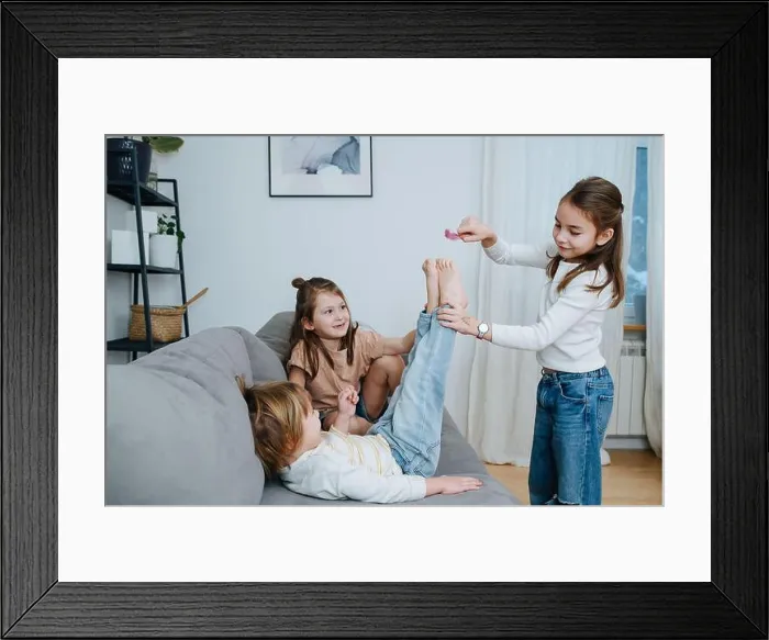 Framed Print : Experimenting girls tickling boy's feet with feather. He straightening his legs towards it, curious about the sensation Framed Print : Experimenting girls tickling boy's feet with feather. He straightening his legs towards it, curious about the sensation