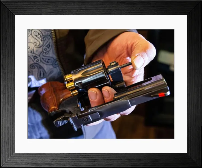 Framed Print : A man ejects spent casings from a black revolver by pushing on the ejector rod Framed Print : A man ejects spent casings from a black revolver by pushing on the ejector rod