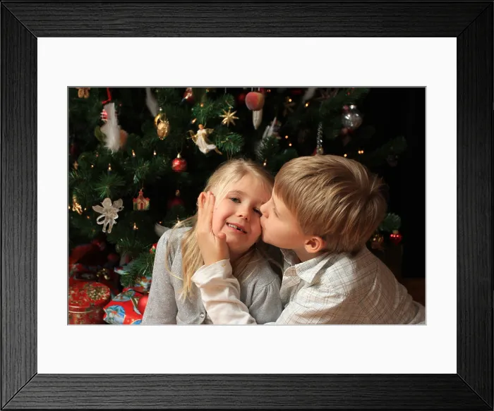 Framed Print : Young boy giving his little sister a kiss in front of a christmas tree with presents below Framed Print : Young boy giving his little sister a kiss in front of a christmas tree with presents below