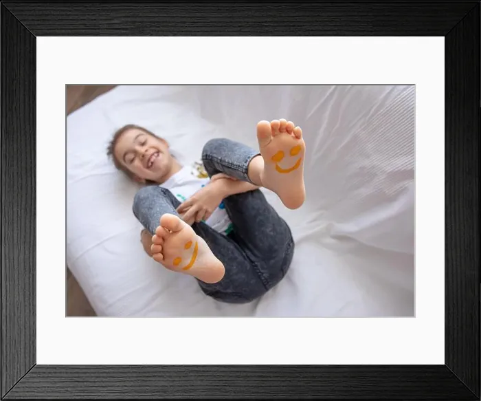 Framed Print : A little girl is lying on a sofa with her feet painted with paints. Funny smiles on children's feet Framed Print : A little girl is lying on a sofa with her feet painted with paints. Funny smiles on children's feet