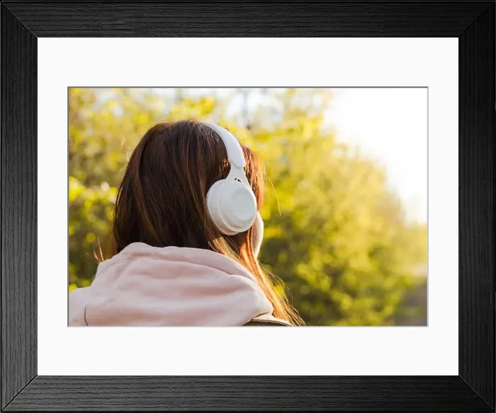 Framed Print : Back view of caucasian young woman listening music with headphones on a sunny day while walking in city park