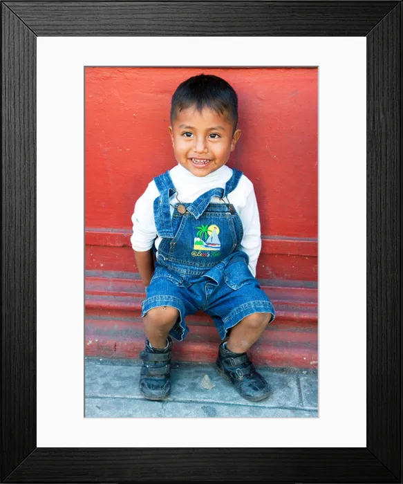 Framed Print : mischievous bright eyed smiling little Mexican boy sits outside against deep red wall on a street in Oaxaca de Juarez Framed Print : mischievous bright eyed smiling little Mexican boy sits outside against deep red wall on a street in Oaxaca de Juarez