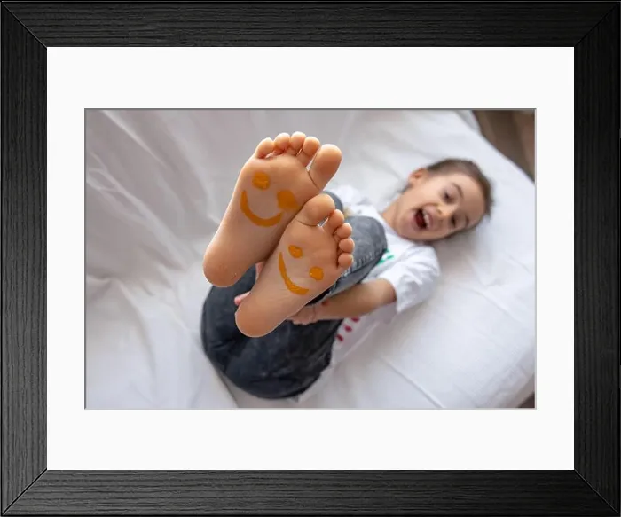 Framed Print : A little girl is lying on a sofa with her feet painted with paints. Funny smiles on children's feet Framed Print : A little girl is lying on a sofa with her feet painted with paints. Funny smiles on children's feet