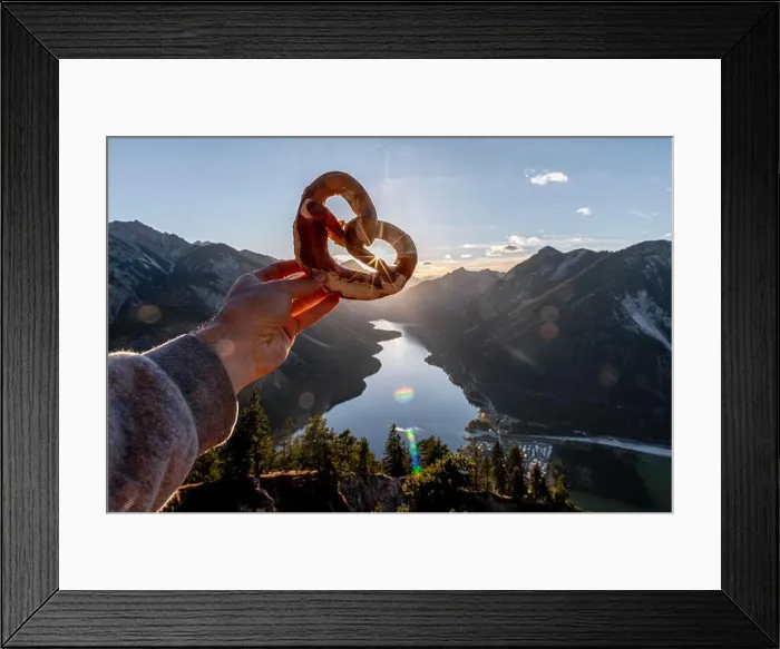 Framed Print : Hand holding Bavarian pretzel in front of Alpine panorama, view from Schonjochl to Plansee, Tyrol, Austria Framed Print : Hand holding Bavarian pretzel in front of Alpine panorama, view from Schonjochl to Plansee, Tyrol, Austria