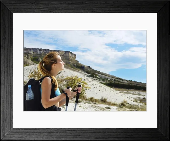 Framed Print : Young woman with backpack and trekking poles in mountains Framed Print : Young woman with backpack and trekking poles in mountains