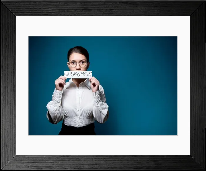 Framed Print : girl in glasses and a white shirt closes her mouth with a piece of paper with the word Harassment Framed Print : girl in glasses and a white shirt closes her mouth with a piece of paper with the word Harassment