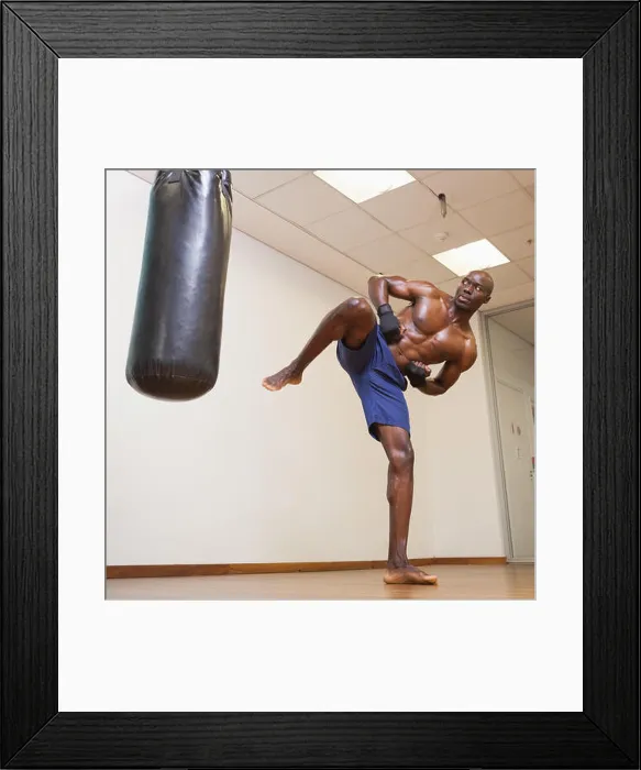Framed Print : Full length of a shirtless muscular boxer kicking punching bag in gym Framed Print : Full length of a shirtless muscular boxer kicking punching bag in gym