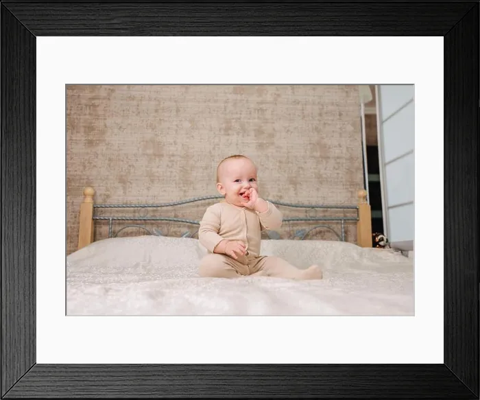 Framed Print : Portrait of cute little baby wearing bodysuit lying on white beedsheets at home Framed Print : Portrait of cute little baby wearing bodysuit lying on white beedsheets at home