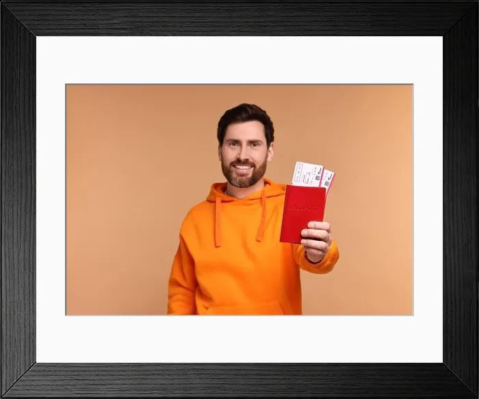 Framed Print : Smiling man showing passport and tickets on beige background Framed Print : Smiling man showing passport and tickets on beige background
