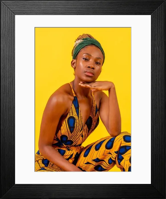 Framed Print : Young african woman with traditional costume on yellow background, sitting looking at camera Framed Print : Young african woman with traditional costume on yellow background, sitting looking at camera