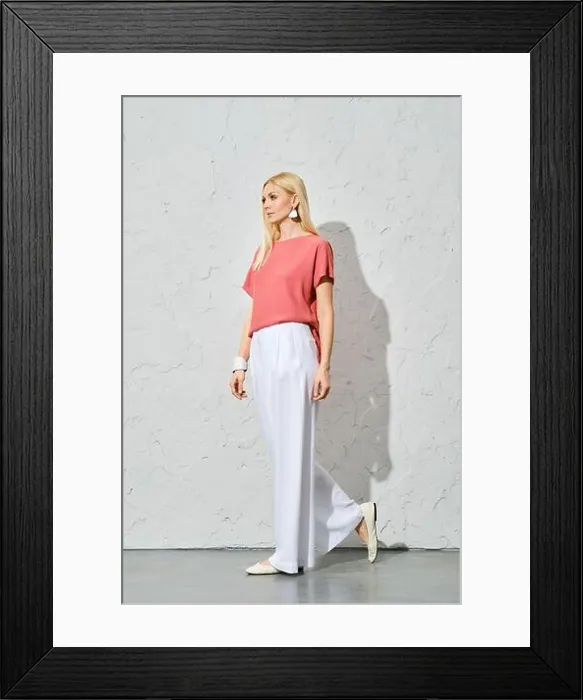 Framed Print : Trendy woman with blond hair in pink shirt and loose white trousers walking along white wall Framed Print : Trendy woman with blond hair in pink shirt and loose white trousers walking along white wall